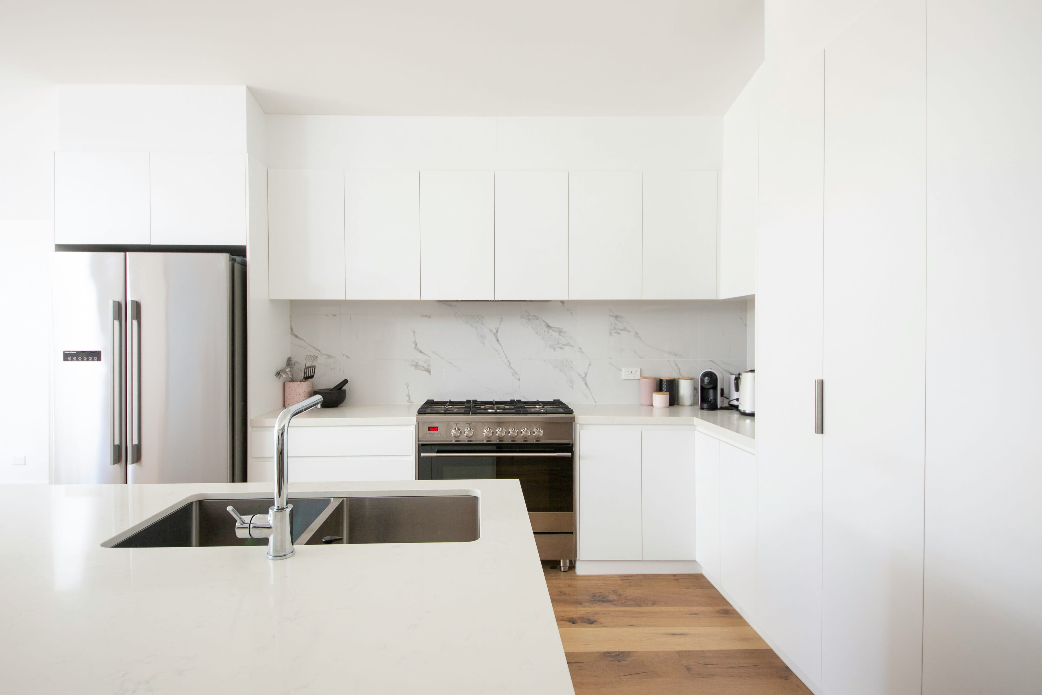 White minimal kitchen with marble look splashback, stainless steel sink and oak floor