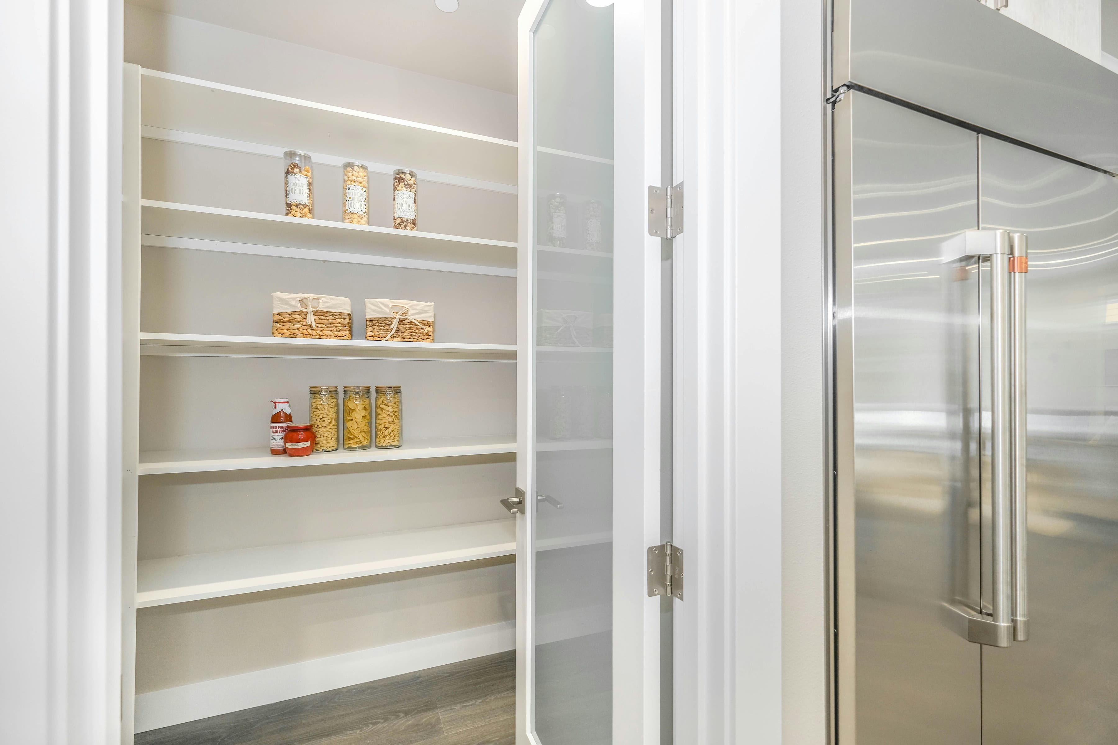 Walk in pantry with white shelves and frosted glass door next to a steel fridge