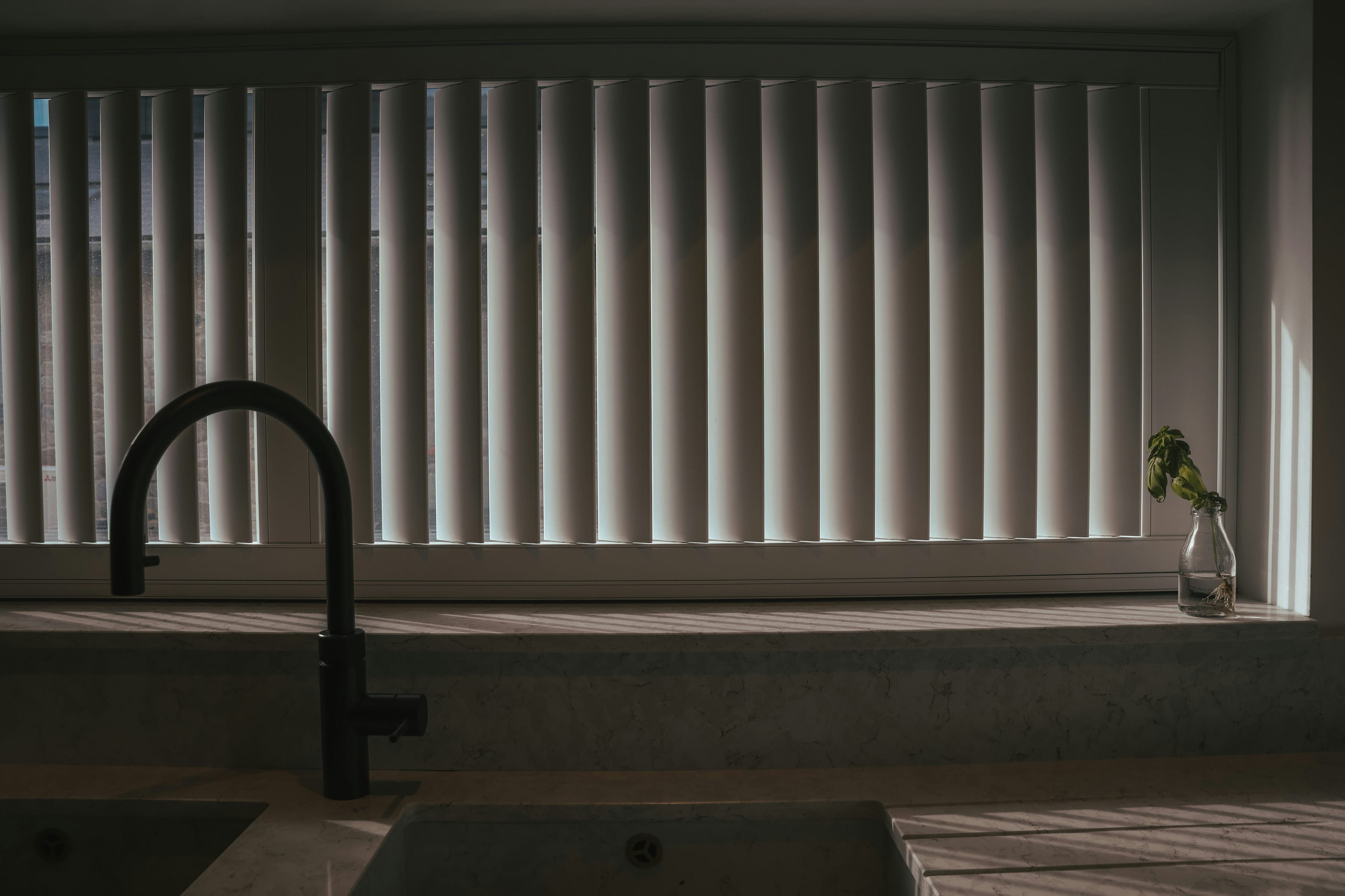 Black arched tap and marble look sill in low sun through a wide louvered window