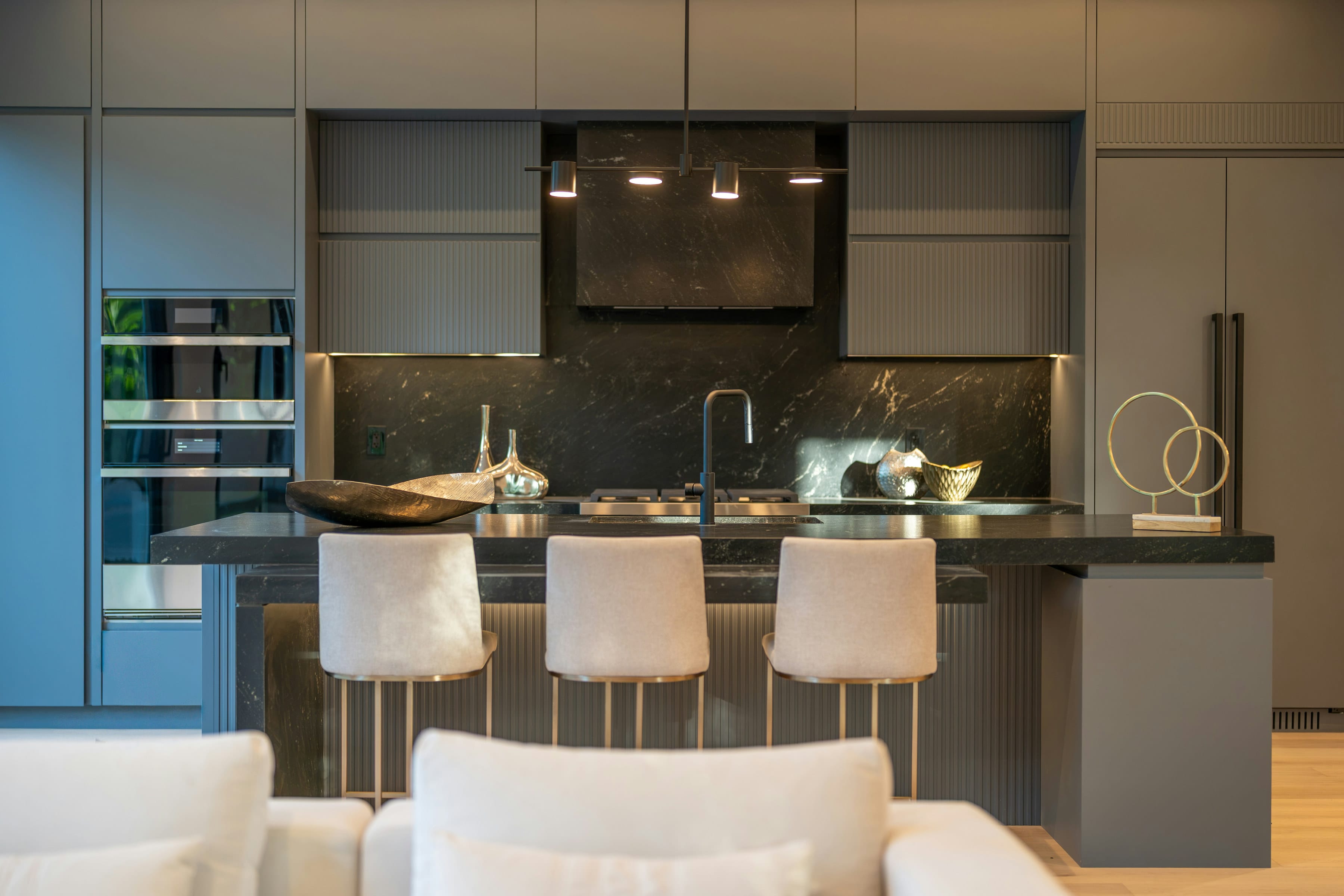 Dark grey island with marble look splashback, pendant lights and cream stools
