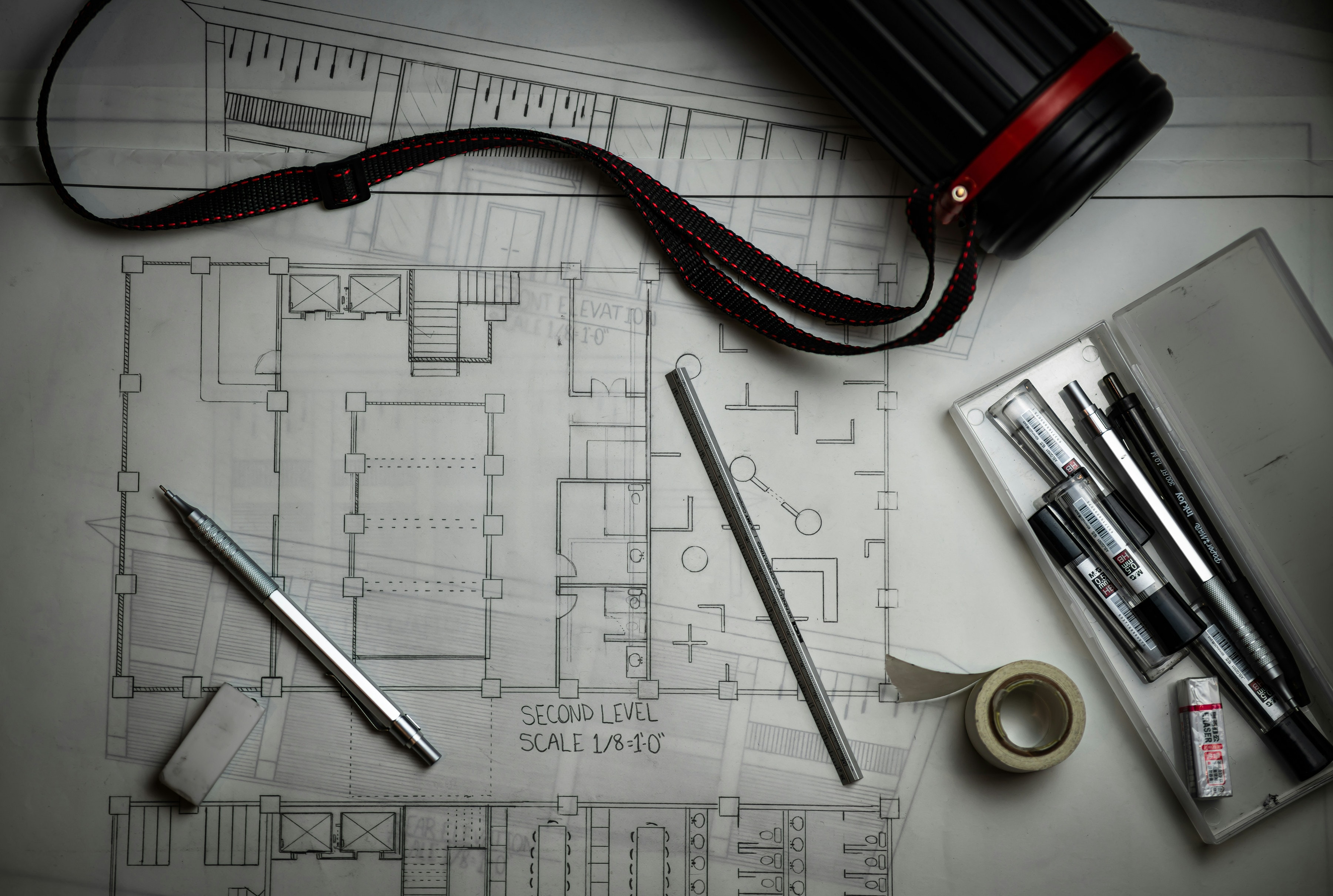 Architectural floor plan with pens, tape and camera strap, flat lay