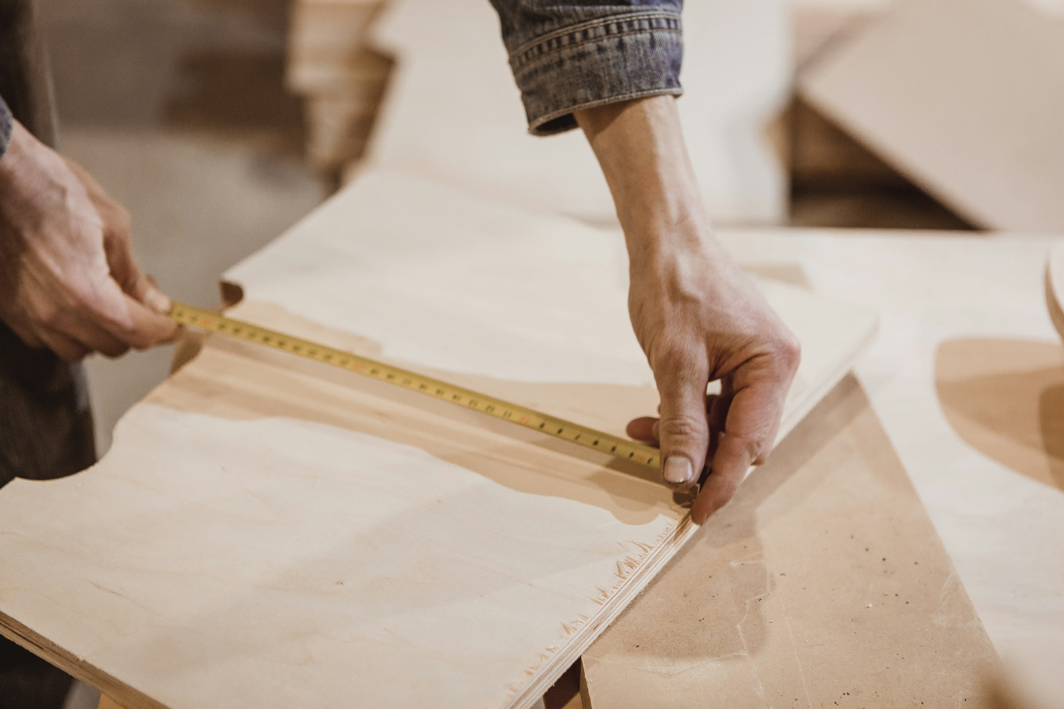 Hands measuring a pale wood veneer sheet with a tape measure