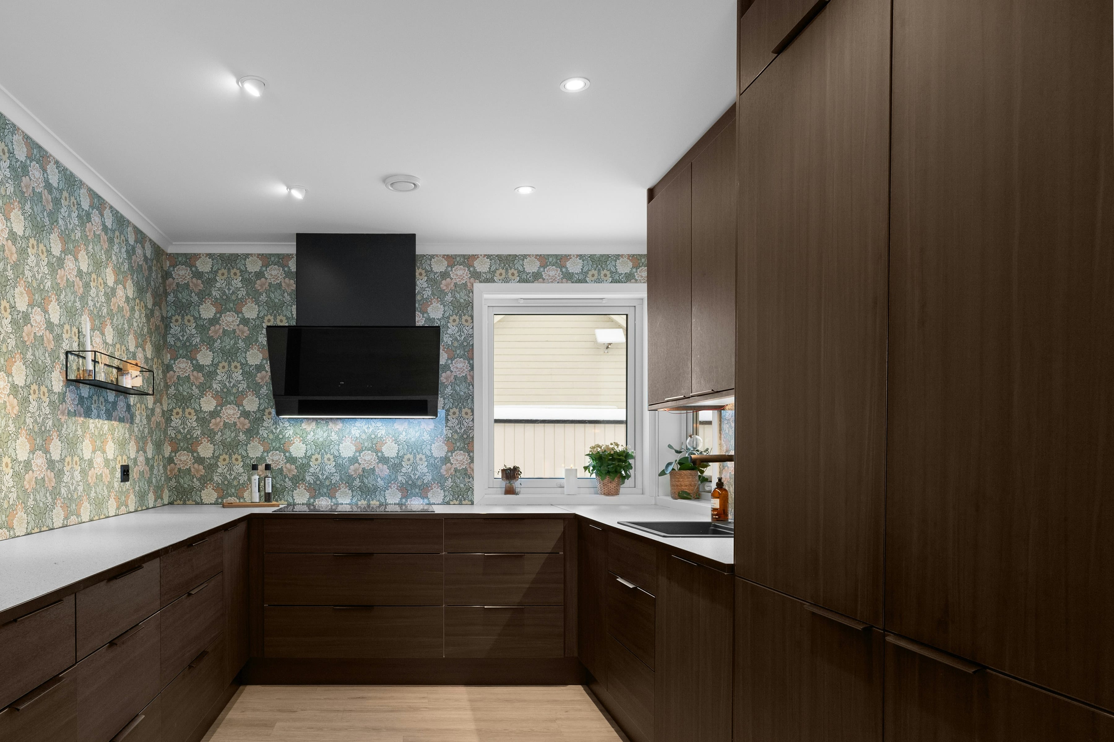 Dark walnut U shaped kitchen with white worktop, oak floor and black hood in the corner