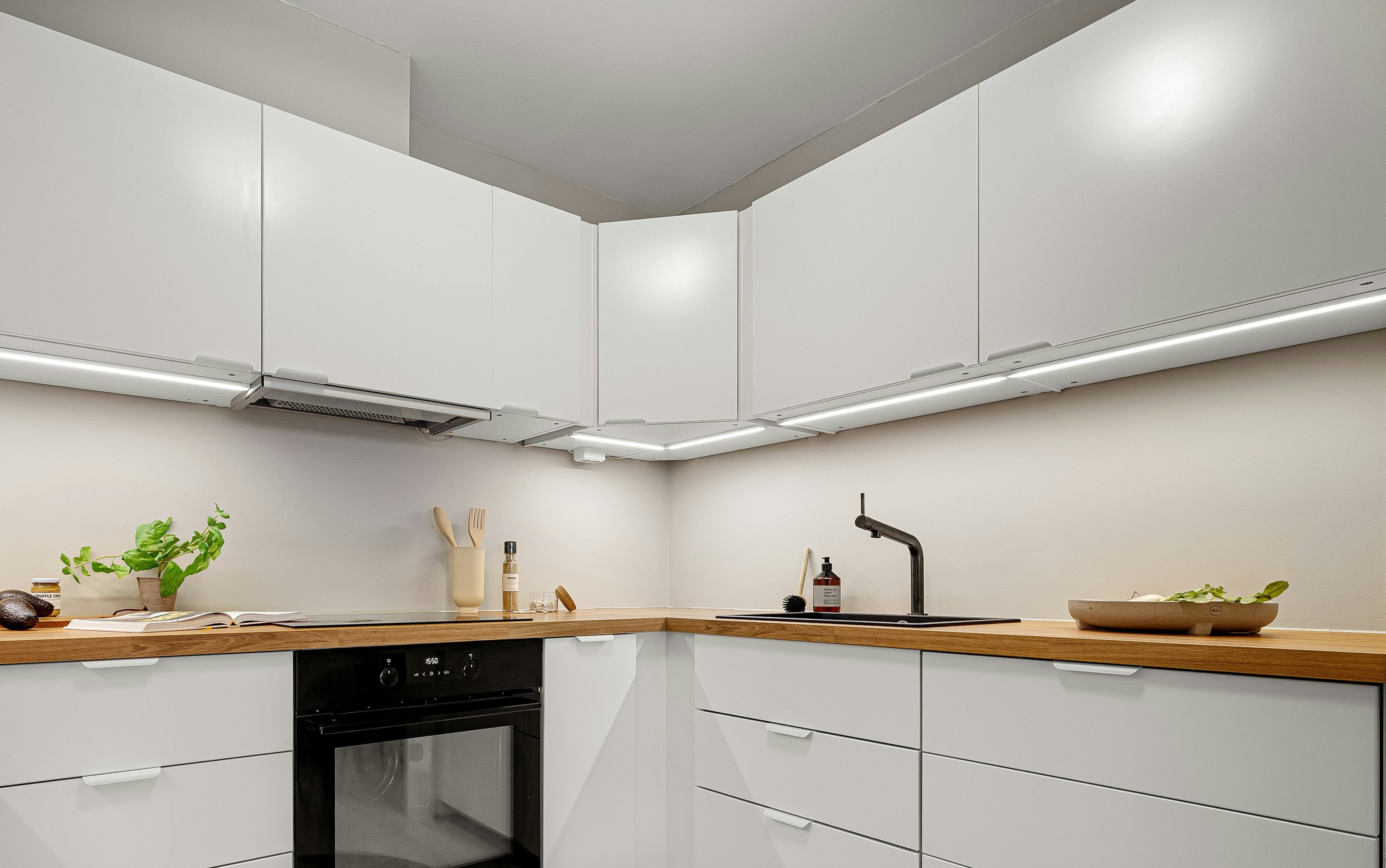 White L shaped kitchen with oak worktop, angled corner wall unit and warm LED strips
