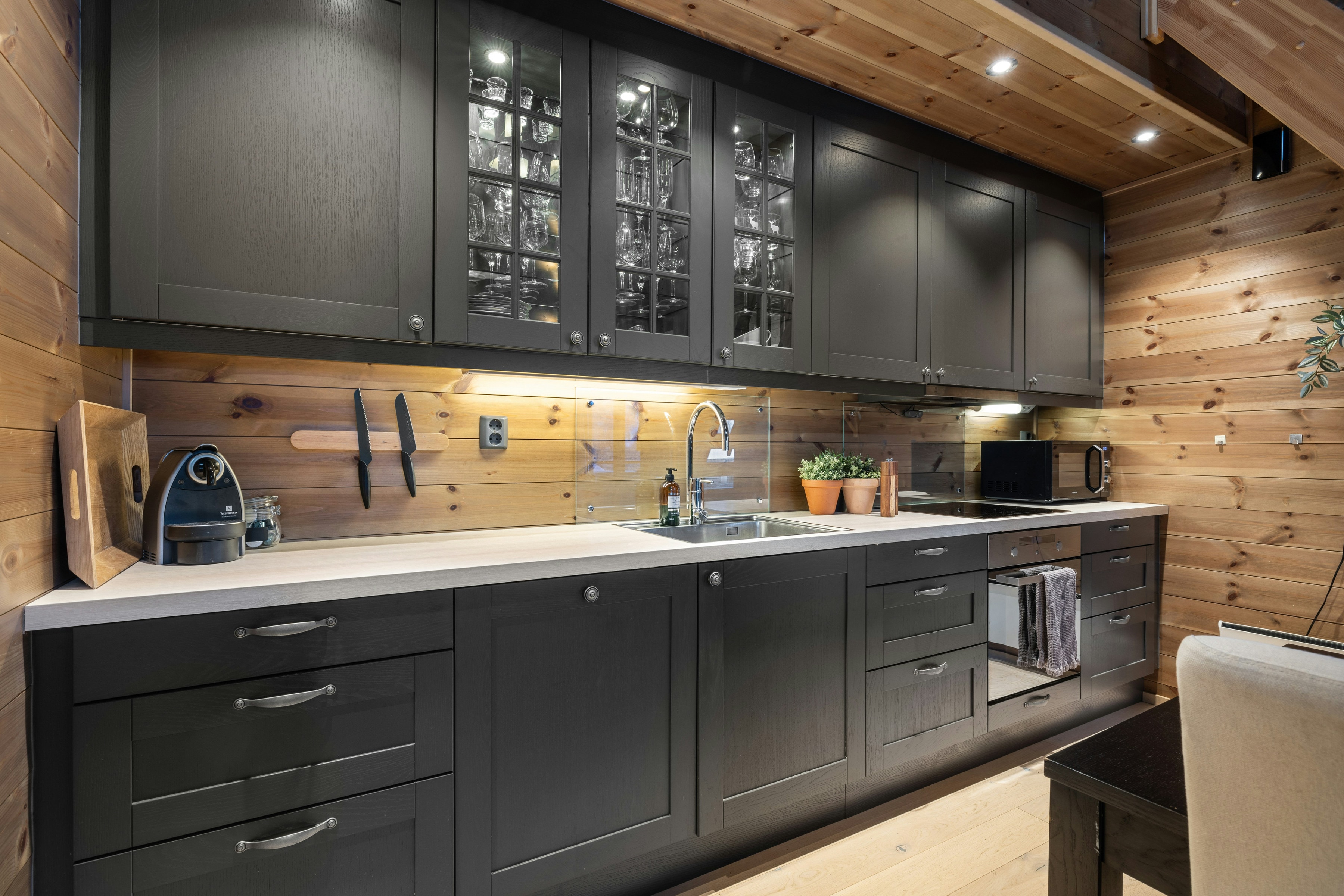 Dark grey kitchen run with glass fronted uppers, warm under cabinet light and knotty pine walls