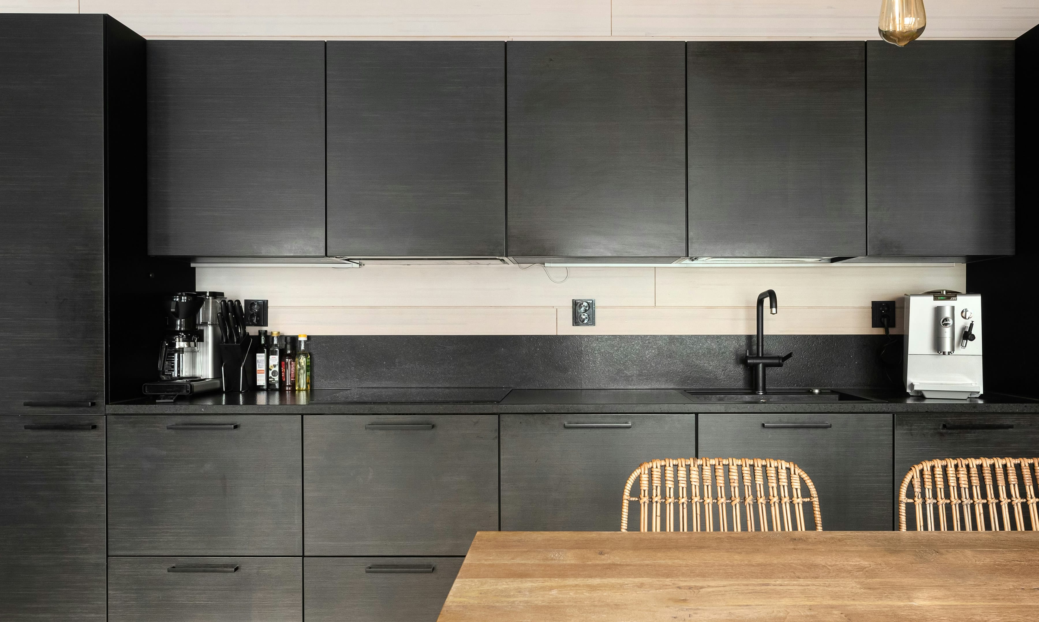 Matt black oak veneer kitchen with black tap, warm pendant bulbs and an oak table in front