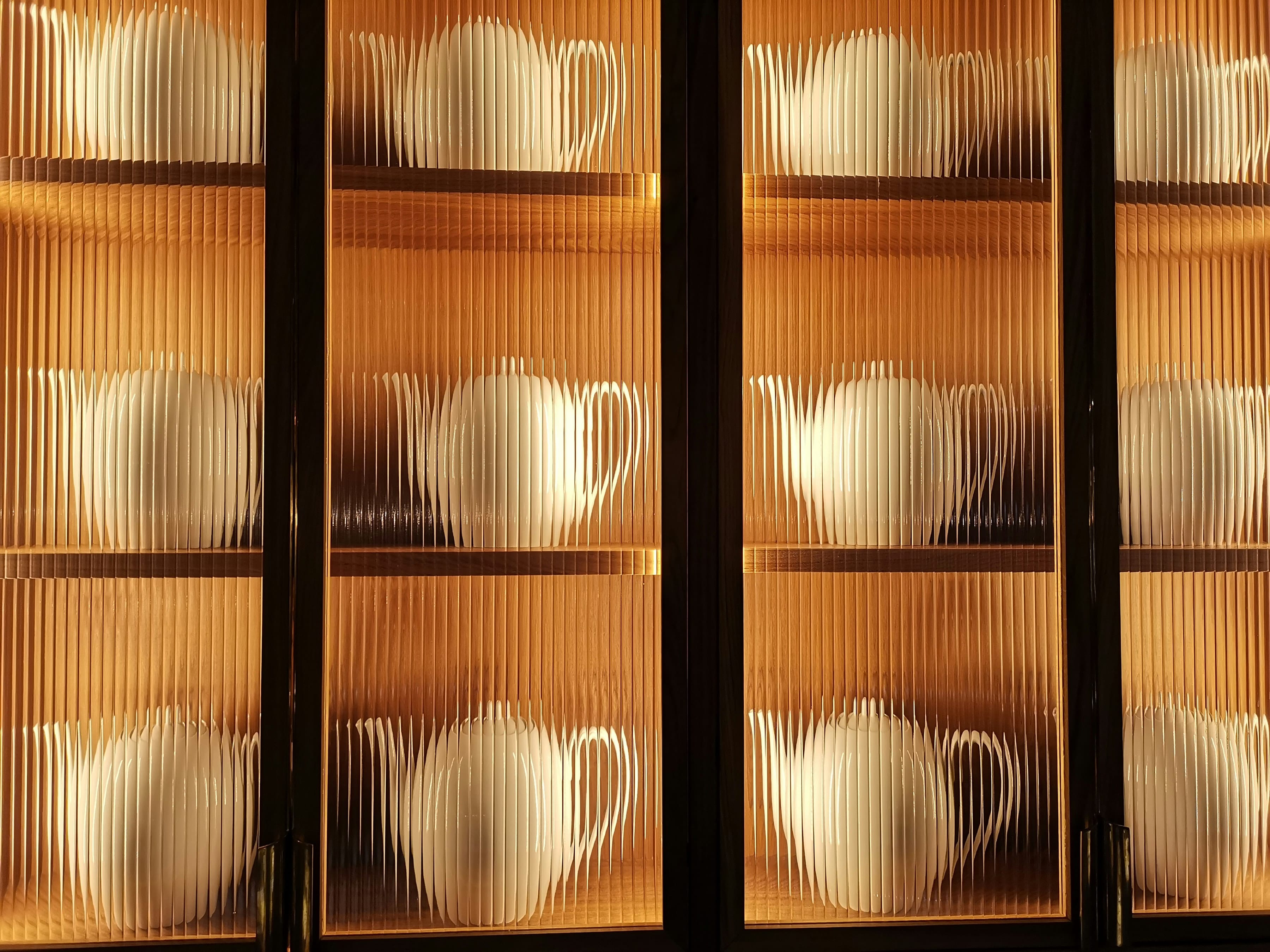 Dark framed fluted glass cabinet doors lit warm from inside, white teapots on oak shelves