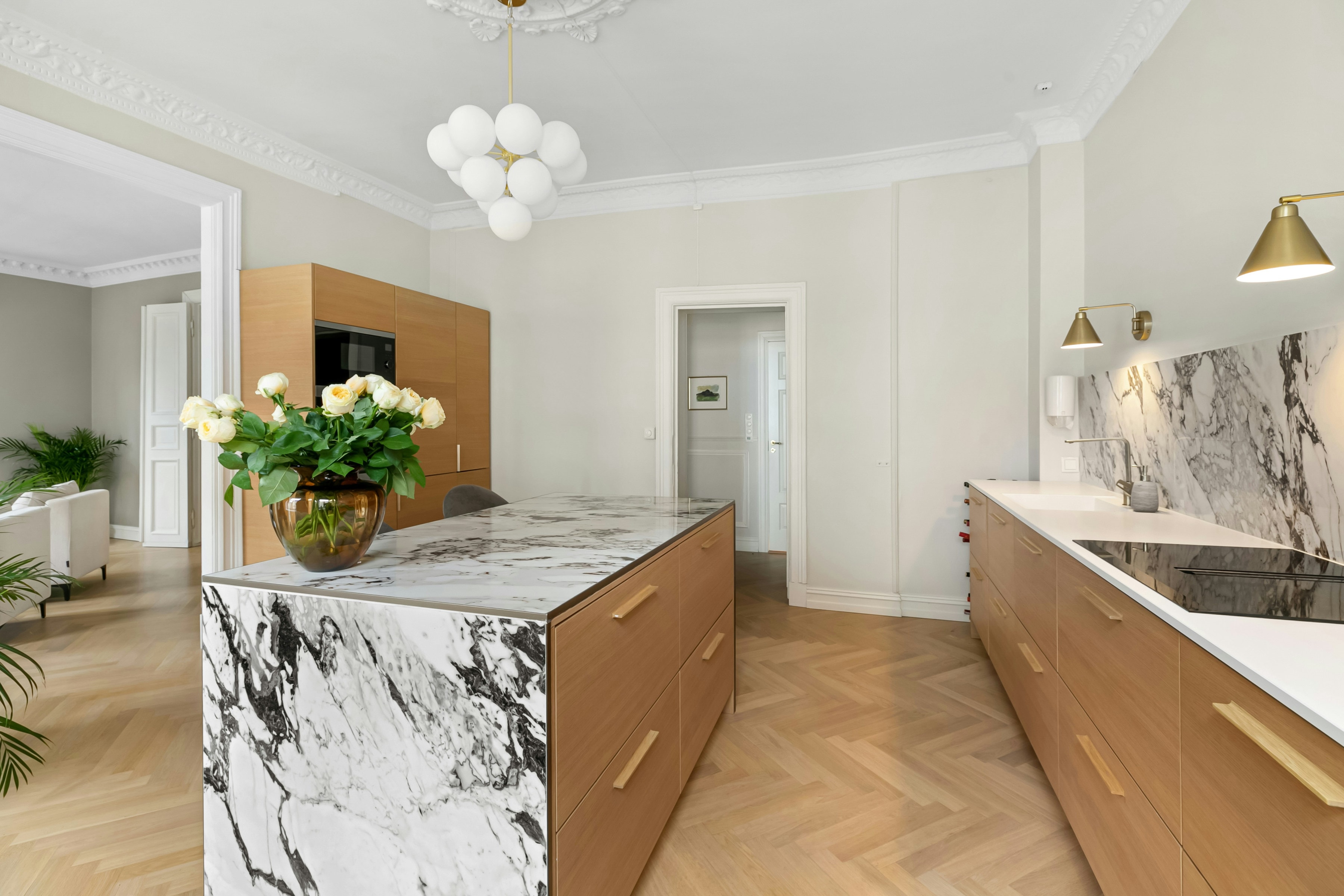 Dramatic marble look waterfall island, oak cabinets with brass pulls and herringbone floor in a classic apartment