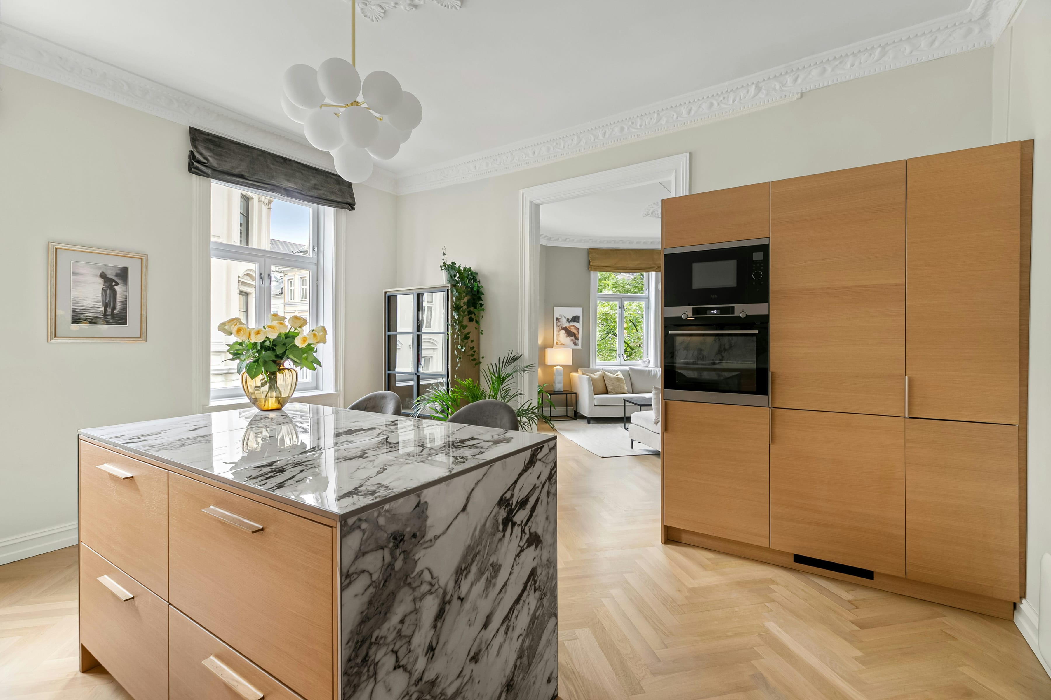 Marble look waterfall island beside a tall oak cabinet wall with built in oven in a bright apartment