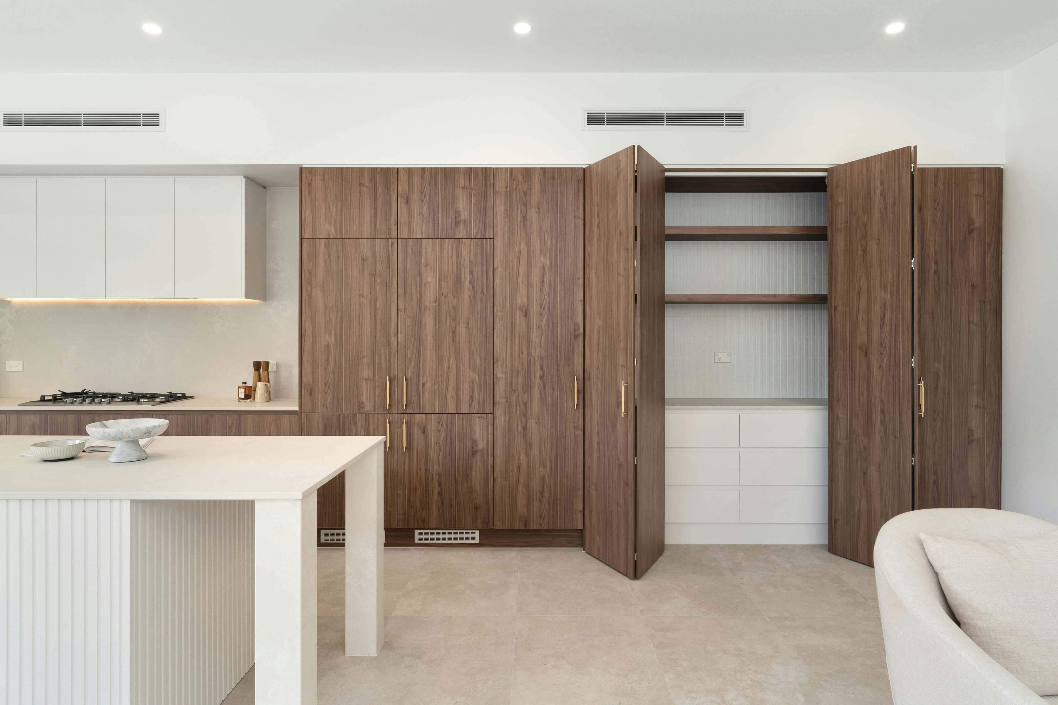 Walnut bi fold doors open to concealed shelving and white drawers inside an open plan kitchen