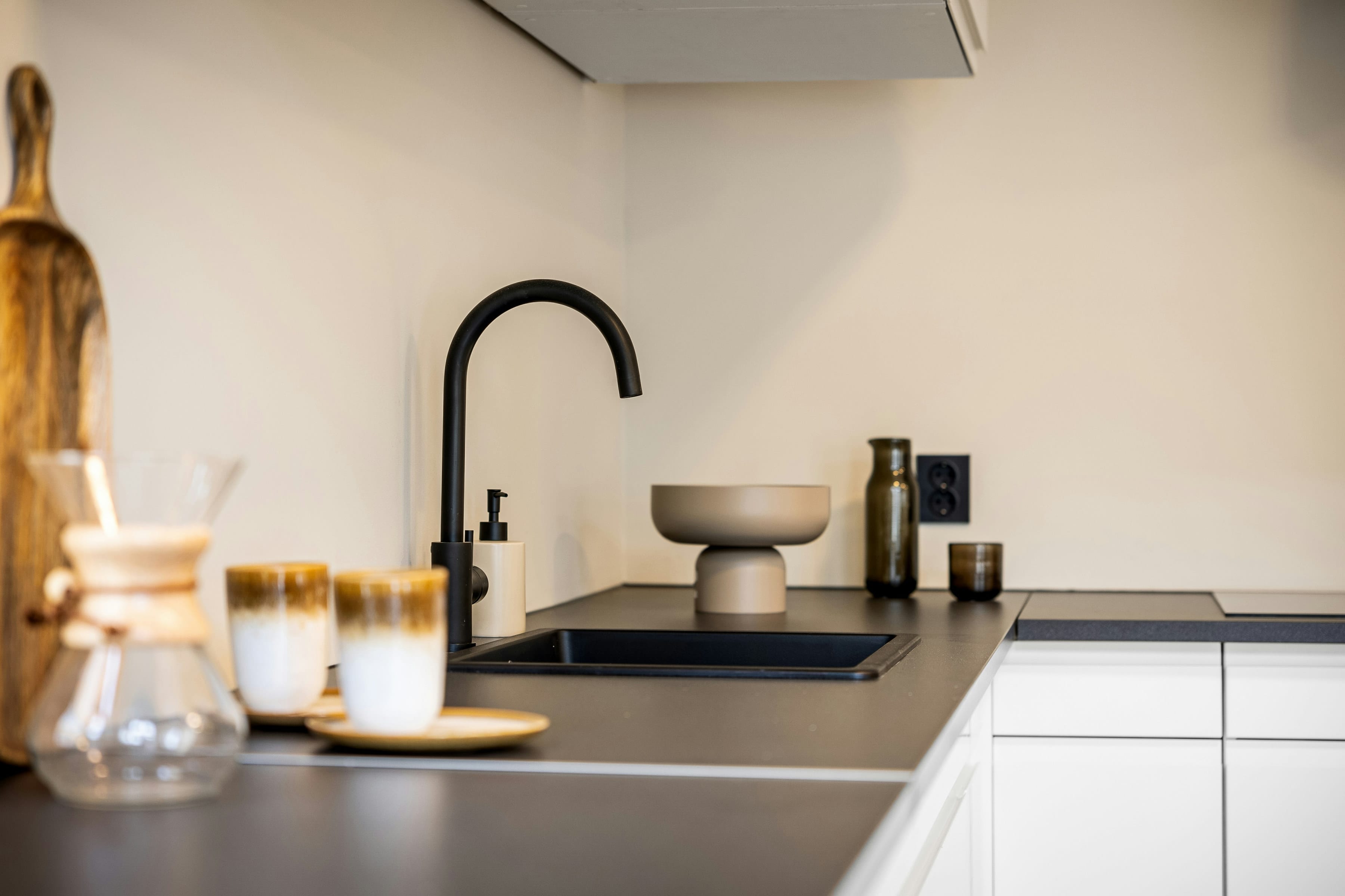 Black swan neck tap and black sink on a dark worktop, ceramic cups in soft foreground
